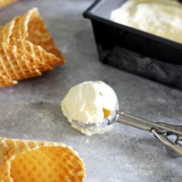 Scoop of no churn vanilla ice-cream with container of ice-cream and waffle cones