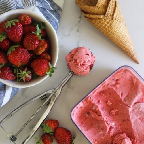 Scoop of strawberry ice cream, cones and strawberries in a bowl