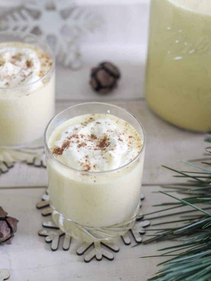 Glasses of eggnog on a tray with pine needles and snowflakes