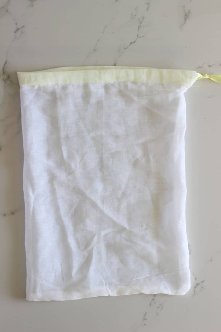 White muslin reusable produce bag with yellow drawstring