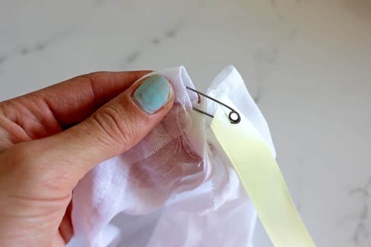 Hand threading a ribbon through top of homemade reusable produce bag