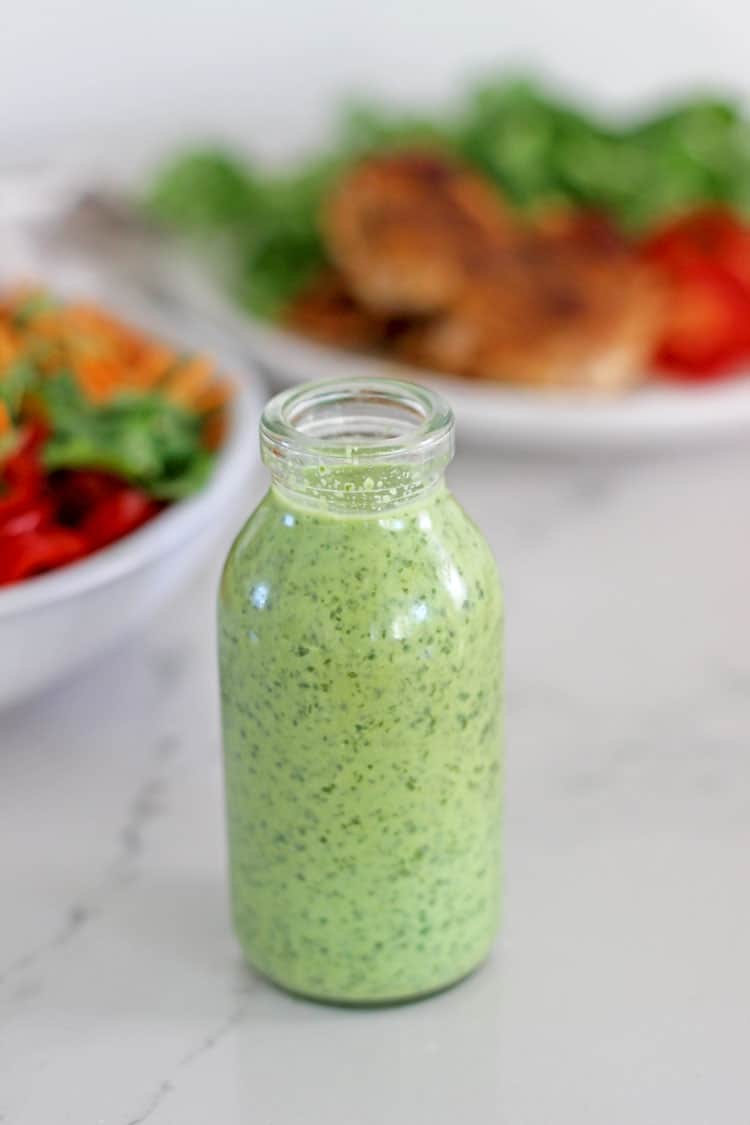Small bottle of cilantro yoghurt dressing with chicken burrito bowl in background