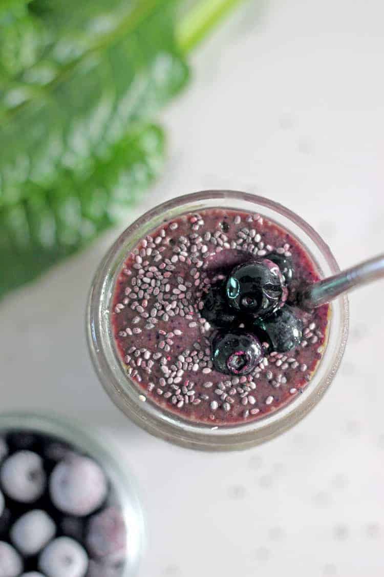 Spinach blueberry smoothie in a glass with metal straw with spinach leaves and blueberries.