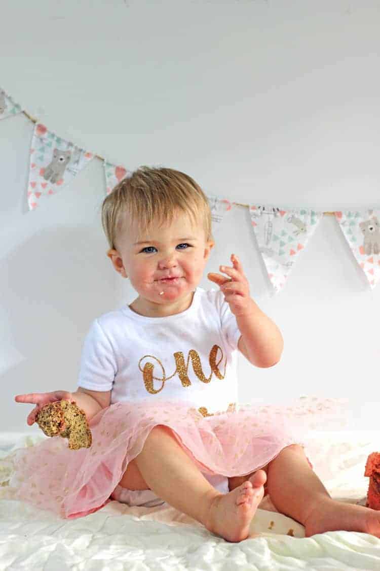 Baby doing a smash cake holding piece of cake in her hand