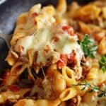 Close up of scoop of cheesy mince pasta with herbs on top
