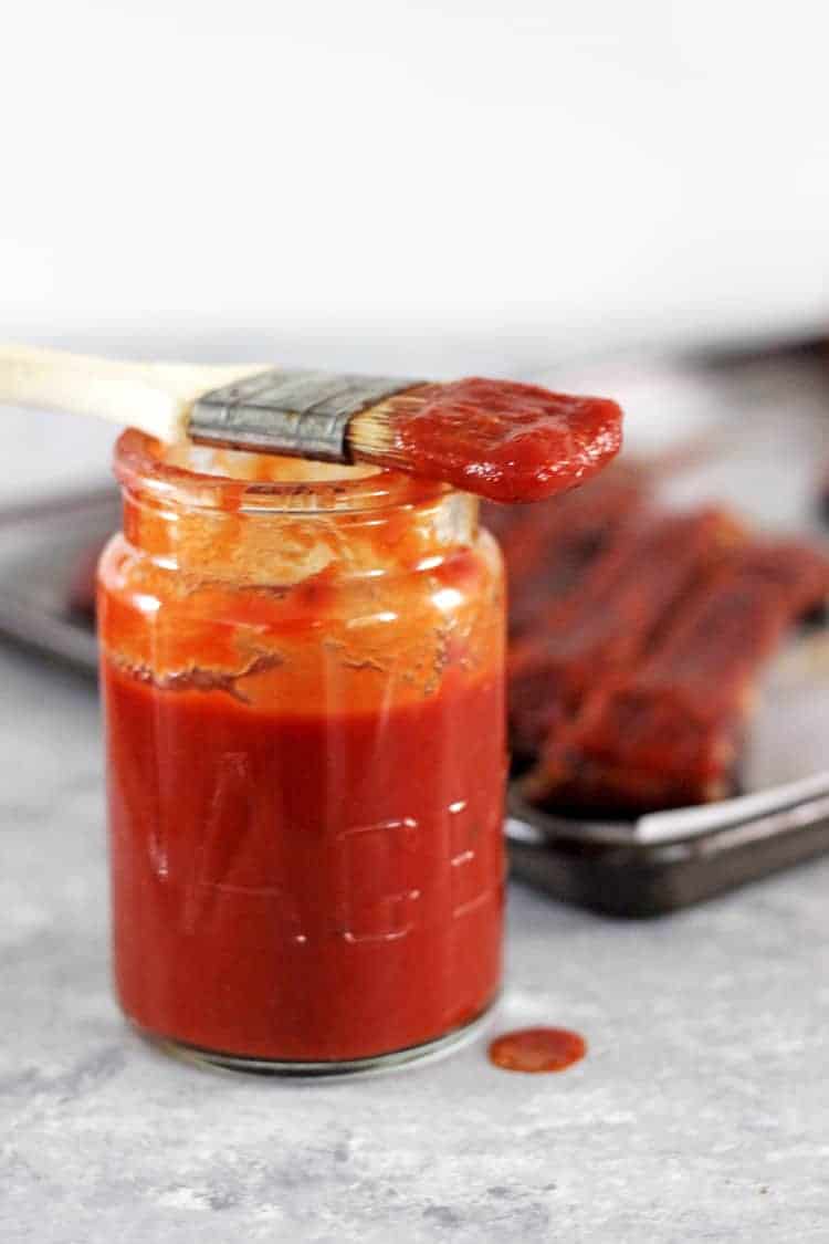 Glass jar of homemade BBQ sauce with pastry brush sitting on top