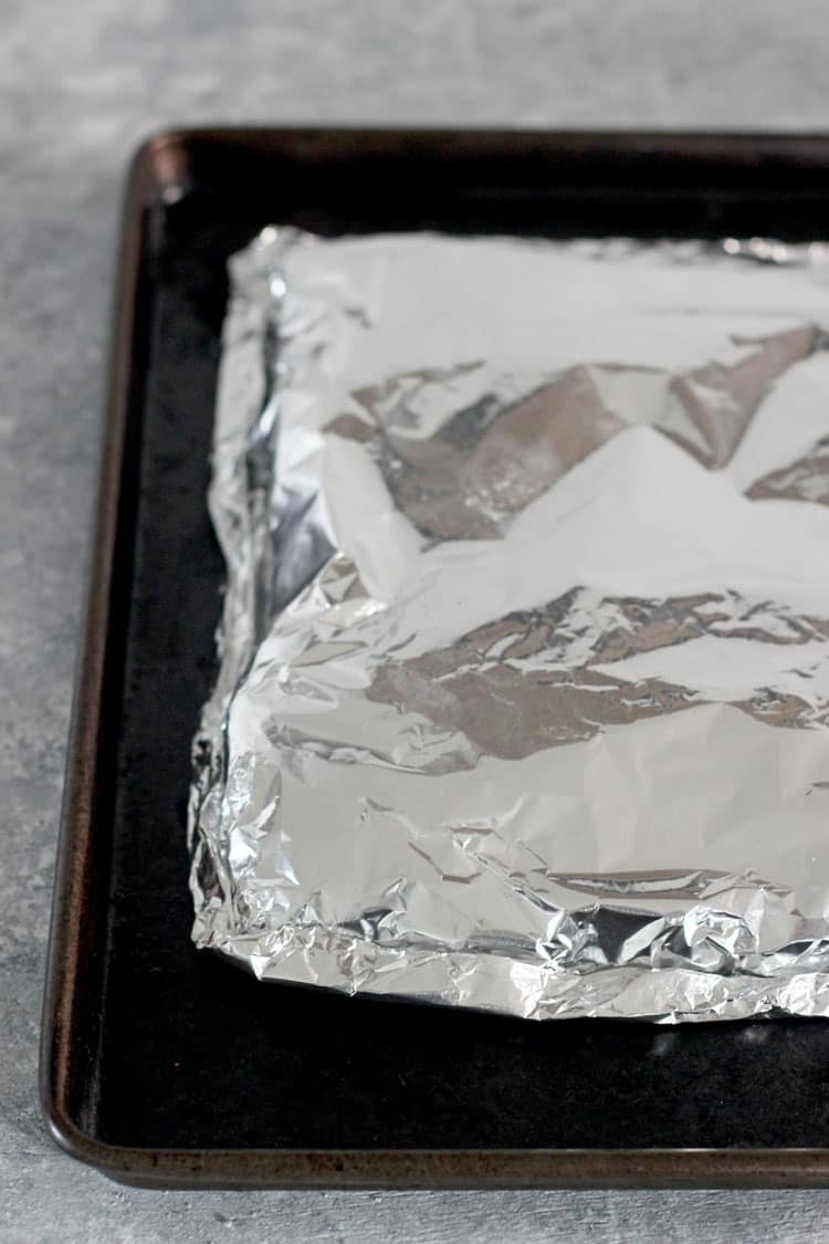 Rack of ribs wrapped in tinfoil on a baking tray