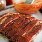 Oven baked pork ribs with bowl of BBQ sauce on an oven tray