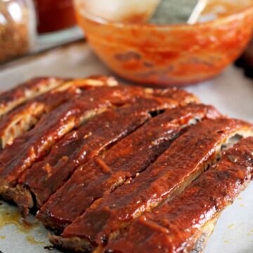 Oven baked pork ribs with bowl of BBQ sauce on an oven tray