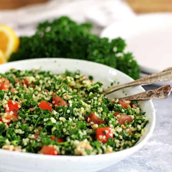 Tabbouleh Salad in a white bowl with fresh parsley and lemons in the background