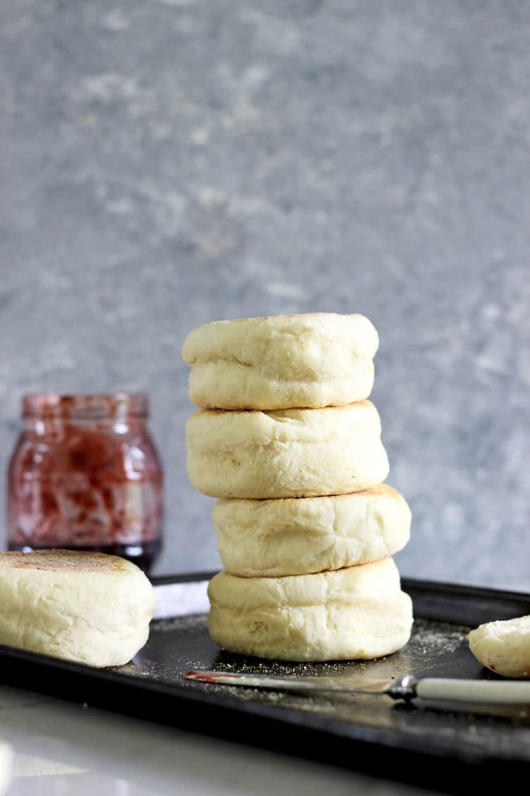 Stack of 4 english muffins on a baking tray with jam jar in background