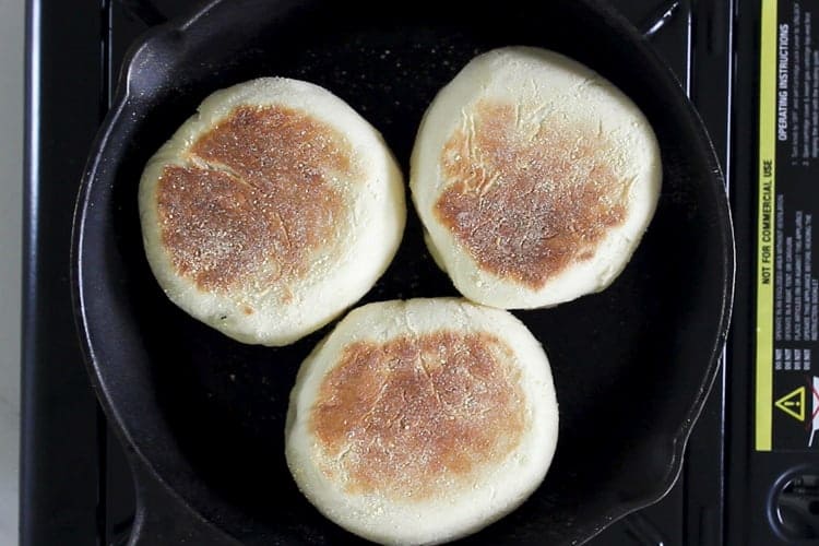 3 english muffins cooking in cast iron frying pan