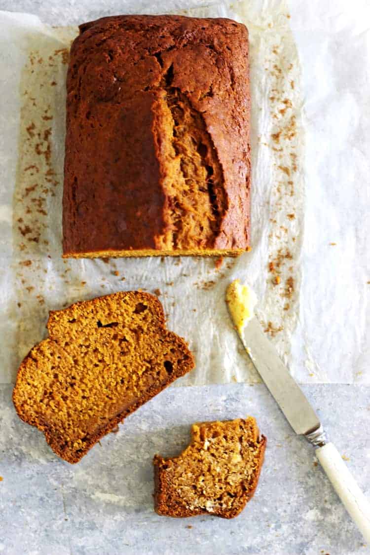 Loaf of pumpkin spice bread from overhead on a white background with 2 slices and a knife with butter
