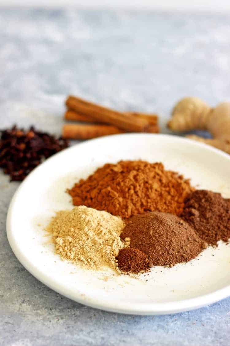 Spices for homemade pumpkin pie spice on a white plate with whole spices in background