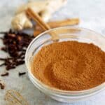 Glass bowl of homemade pumpkin pie spice with whole spice ingredients in the background