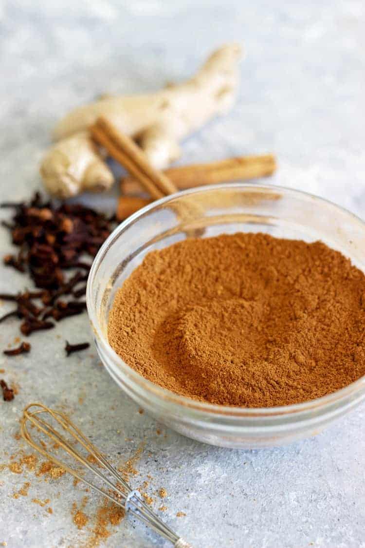 Glass bowl of homemade pumpkin pie spice with whole spice ingredients in the background