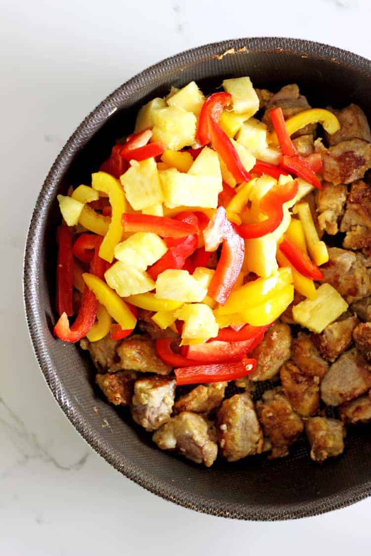 Close up of sweet and sour pork in frying pan with pineapple and pepper added