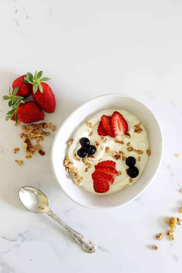 Bowl of yoghurt with strawberries, granola and a spoon on a white background