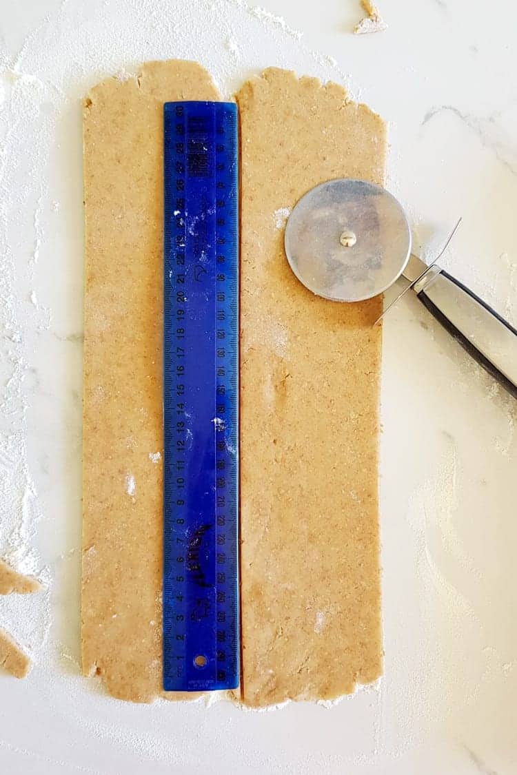 Graham cracker dough rolled out being measured to cut with pizza cutter and ruler