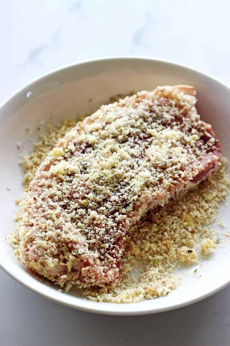 Pork chop being coated in breadcrumb mix