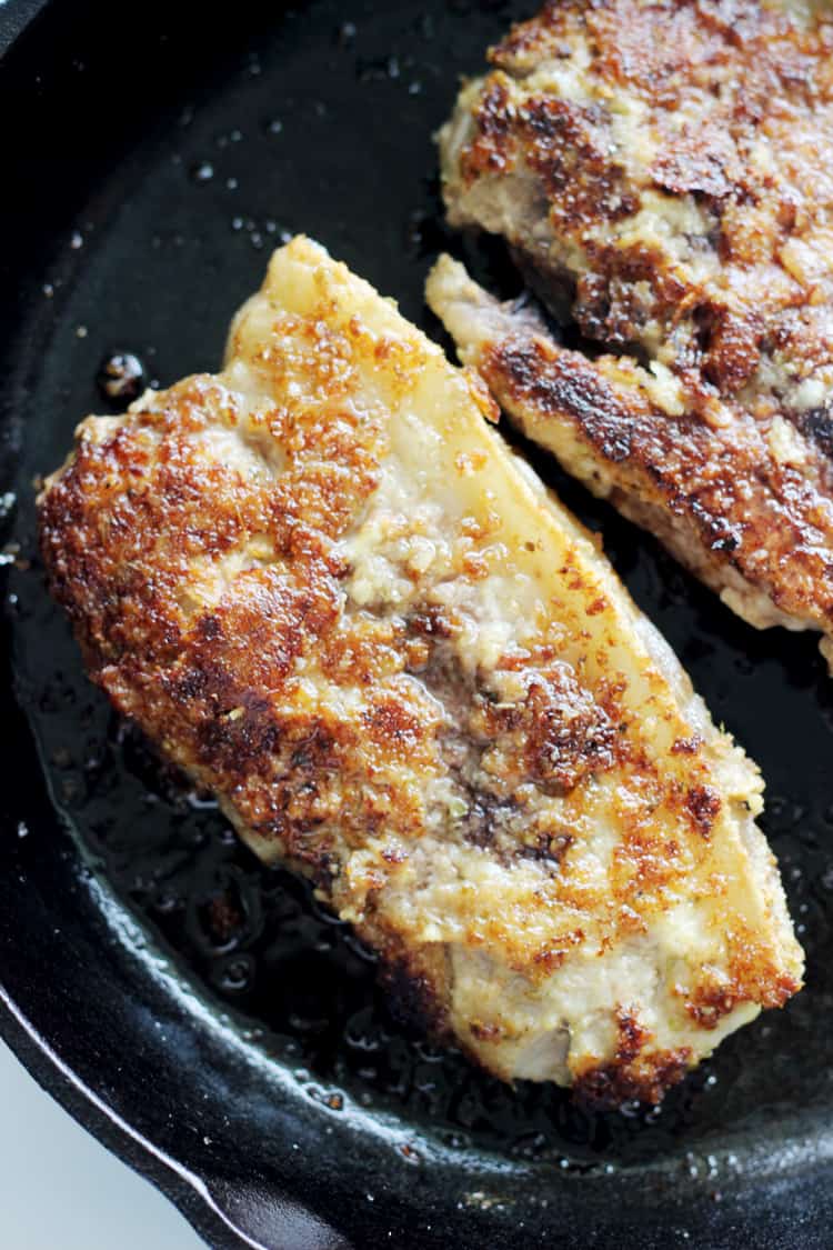 Parmesan pork chops cooking in a cast iron frying pan