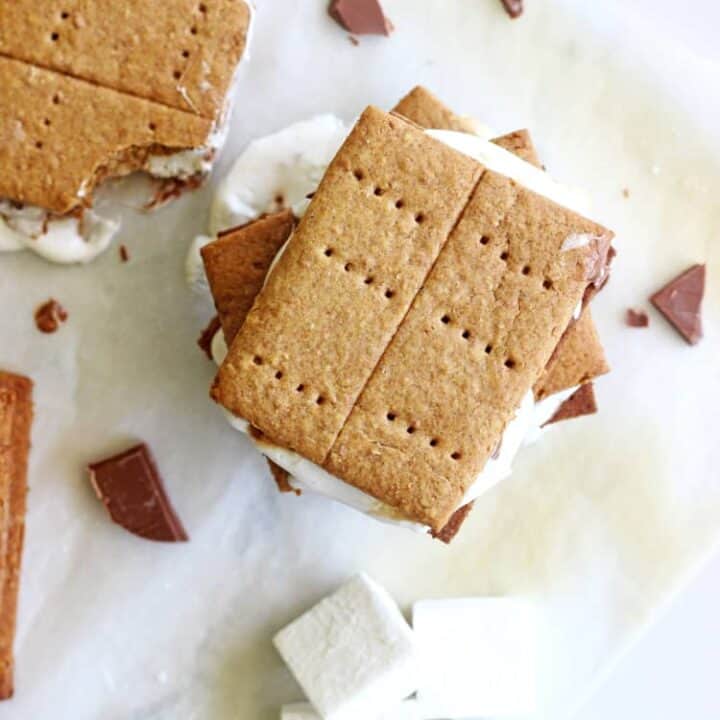 A stack of s'mores on a sheet of baking paper with marshmallows on the side and another s'more with a bite taken out