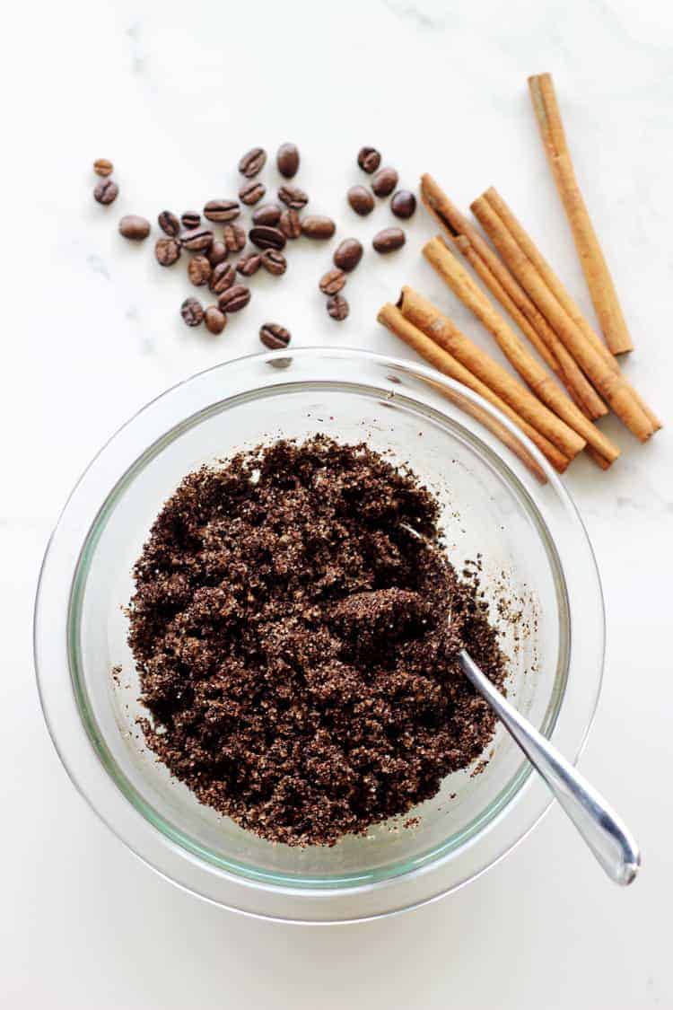 Coffee sugar scrub in a glass bowl with coffee beans and cinnamon sticks on a white background