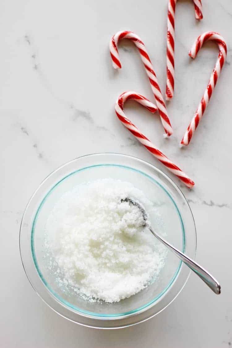Peppermint sugar scrub in a glass bowl with candy canes on a white background