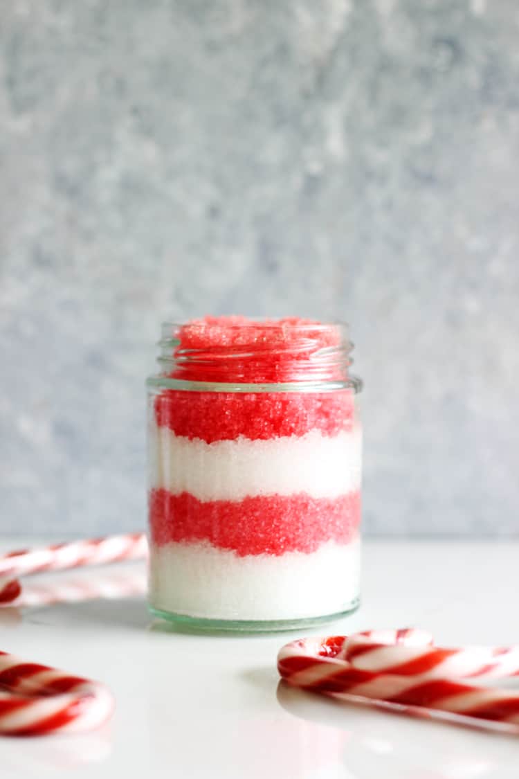 Peppermint sugar scrub in a glass jar with candy canes on a white background