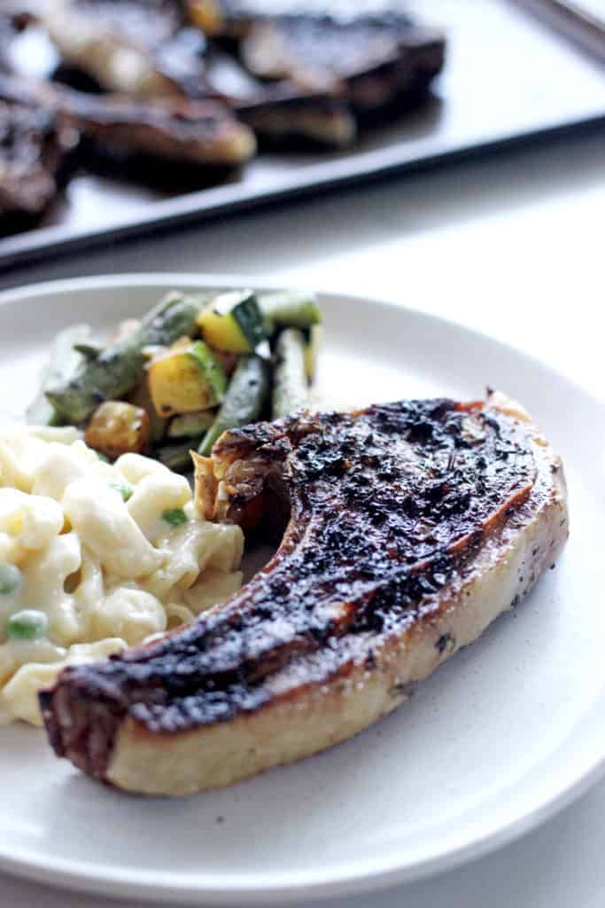 Lamb chops covered in herb marinade on a dinner plate with mac and cheese and veggies