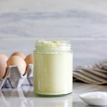 Jar of homemade mayo with eggs, salt and tea towel in background