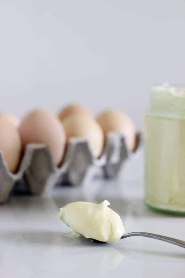 Jar of homemade mayo with spoonful in front and eggs in background