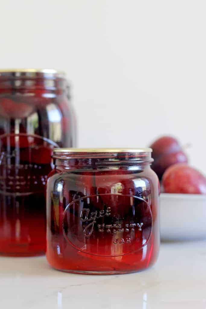 Sealed jars of bottled plums with bowl of plums in background