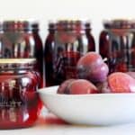 Sealed jars of bottled plums with bowl of plums in background