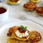 Plate with zucchini fritters topped with sour cream and more fritters in the background