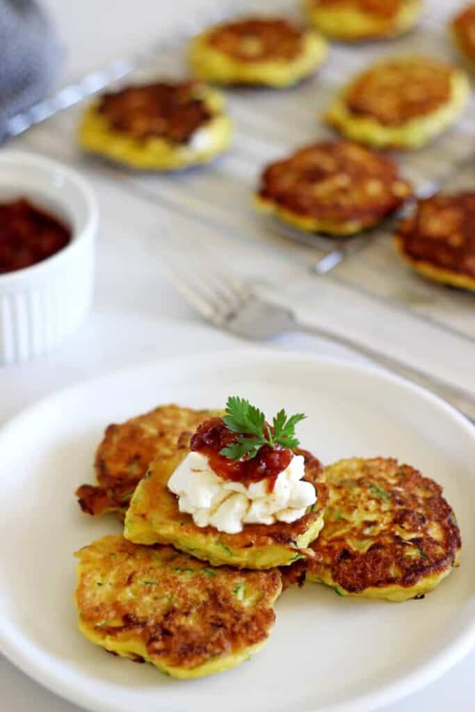 Plate with zucchini fritters topped with sour cream and more fritters in the background