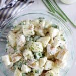 Overhead of bowl with potato salad, chives and tea towel in background