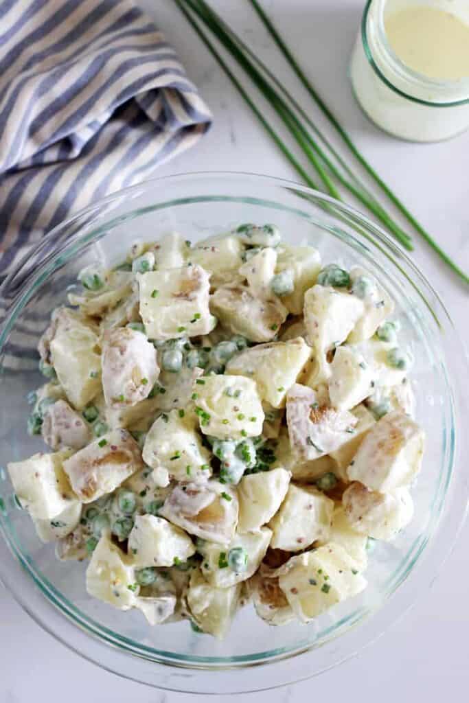 Overhead of bowl with potato salad, chives and tea towel in background