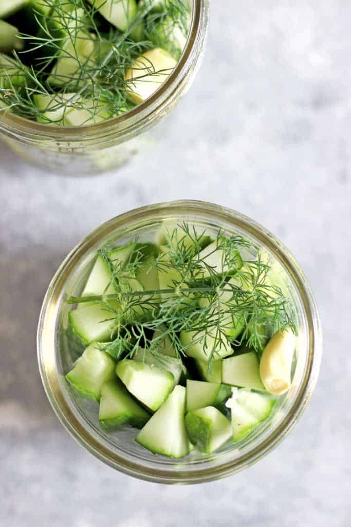 Overhead shot of jars of sliced pickling cucumbers and fresh dill on a grey background