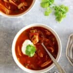 Bowl of Mexican chicken soup topped with sour cream and cilantro on a grey background