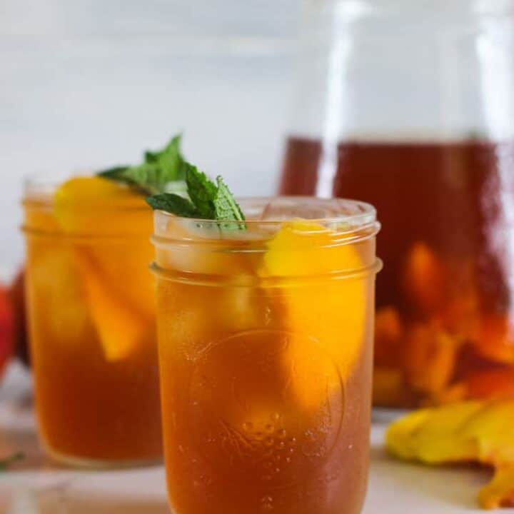 2 glasses of peach iced tea with jug in background