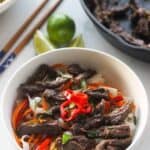 White bowl with beef noodle salad and chopsticks and limes in background