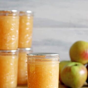 Jar of canned applesauce with apples on wooden background