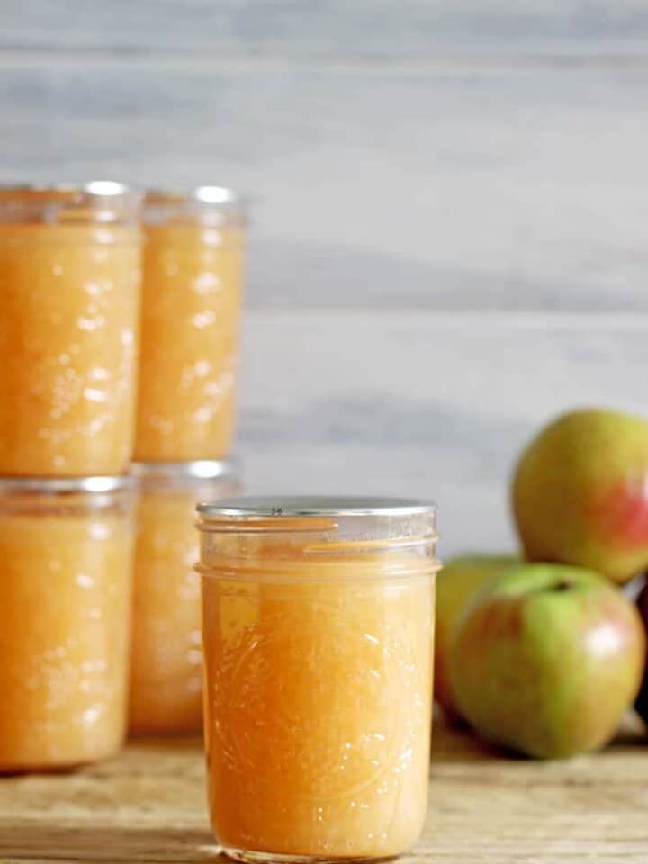 Jar of canned applesauce with apples on wooden background