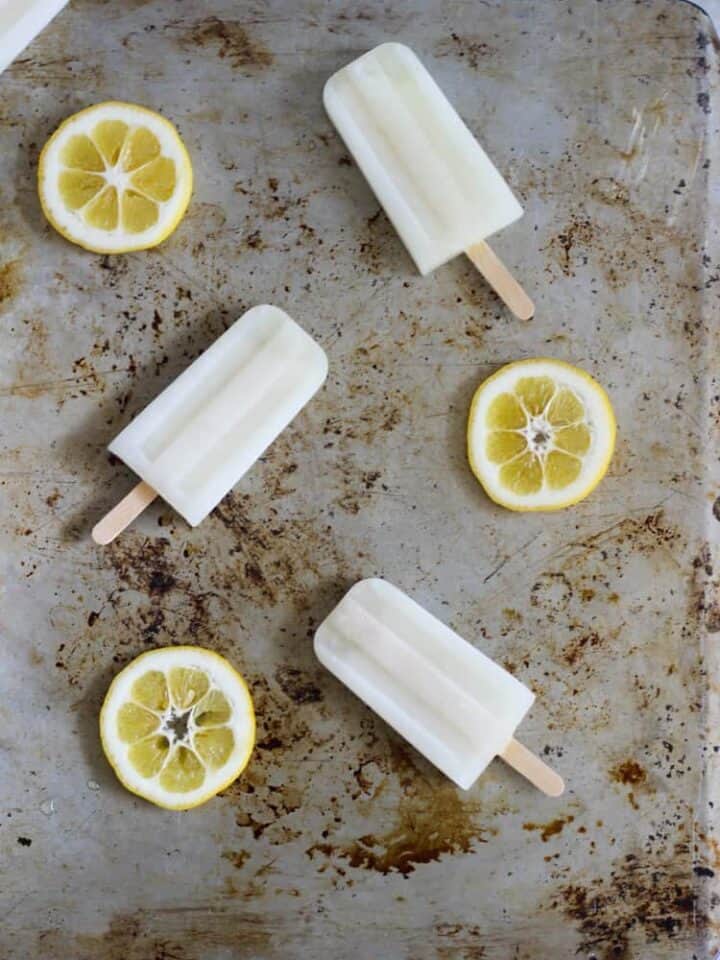 Lemonade popsicles on a baking sheet with lemon slices