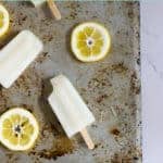 Lemonade popsicles on a baking sheet with lemon slices