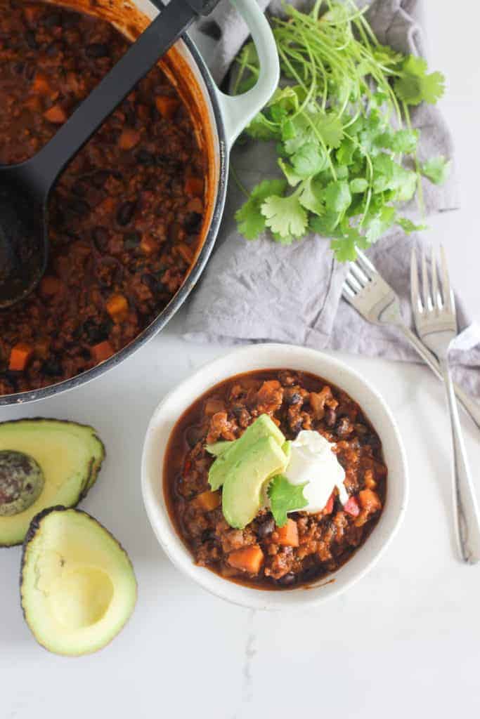 Bowl of chili with avocado, sour cream and pot in background