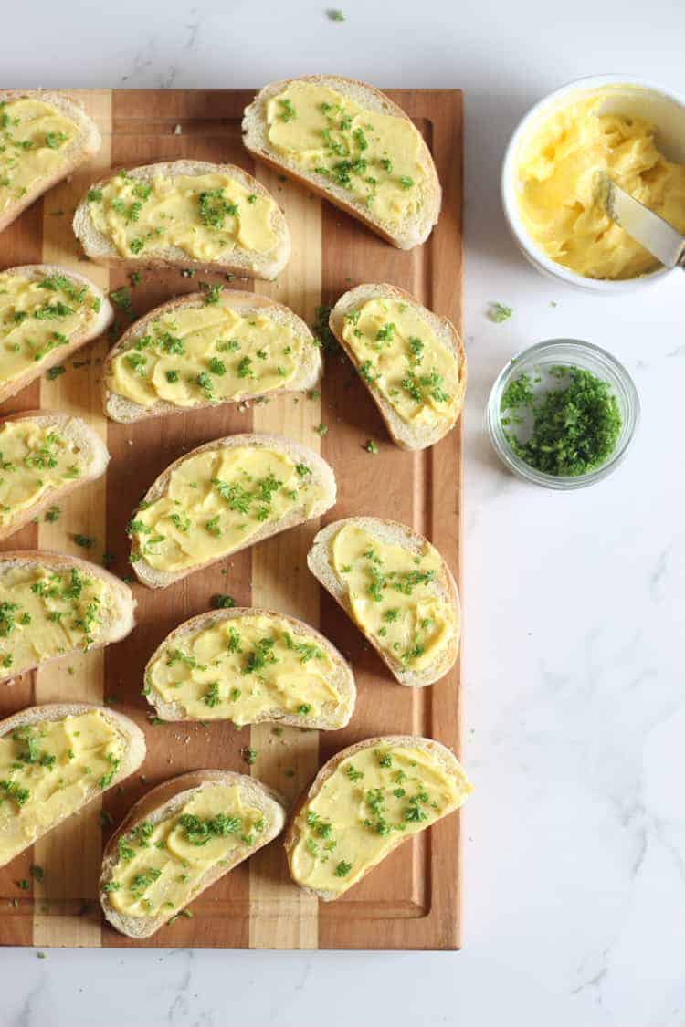 Homemade garlic bread on a chopping board with garlic butter and fresh parsley