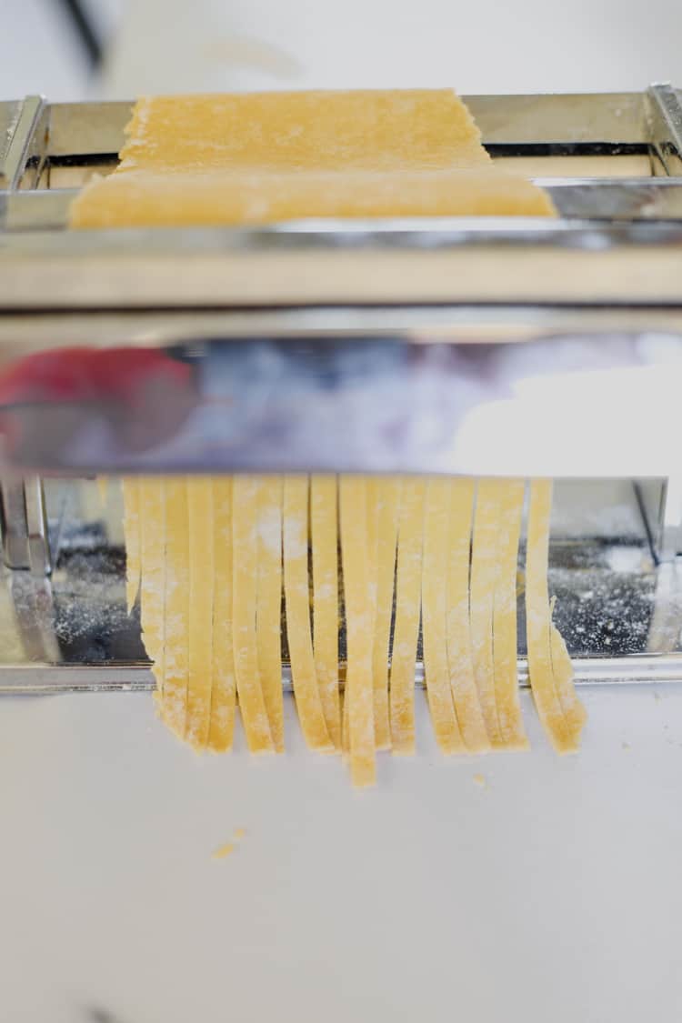 Pasta being rolled through a pasta roller into fettucine