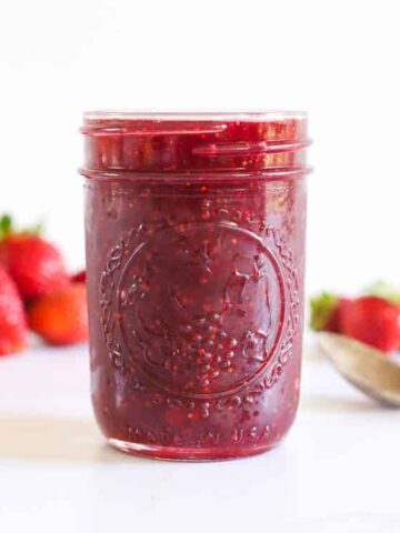 Jar of strawberry jam with strawberries in background and spoon